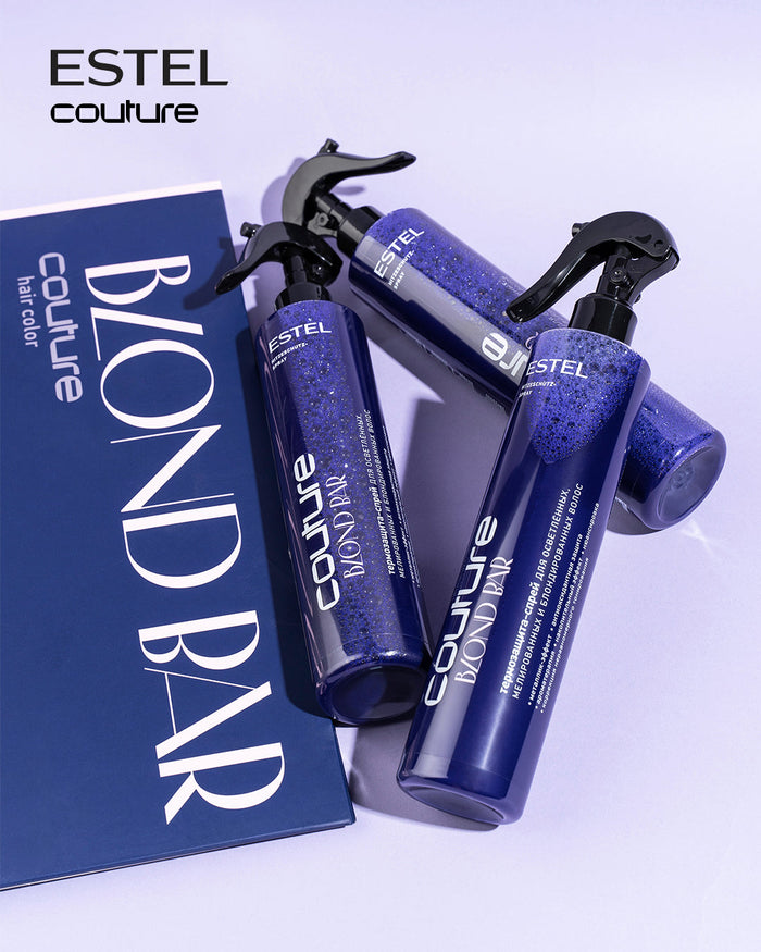 Drei Estel Blond Bar Couture Sprays mit violetter Fluessigkeit neben blauer Verpackung.