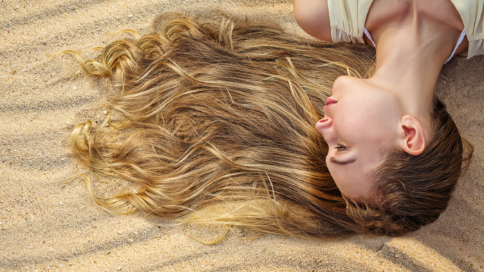 Frau liegt seitlich im Sand, ihr langes blondes Haar ist weit ausgebreitet.