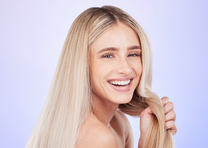 Frau mit langen, glatten blonden Haaren lächelt und hält eine Haarsträhne.
