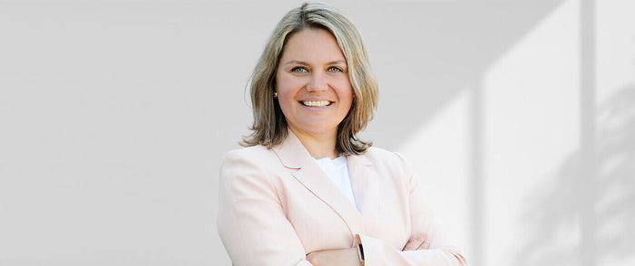 lullia Reinsberger mit hellblondem Haar in hellrosa Blazer lächelt in die Kamera, Arme locker verschränkt.