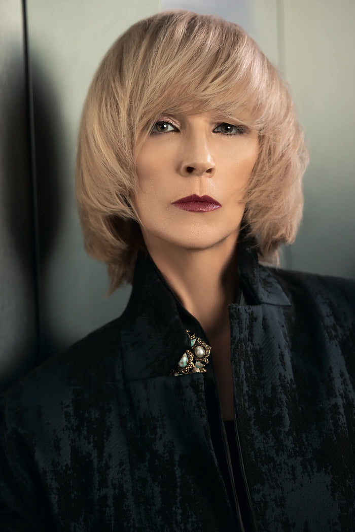 Frau mit mittellangem blondem Haar, trägt dunkles Outfit mit dekorativer Brosche.