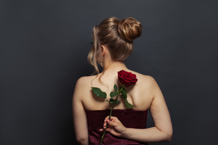 Frau mit elegantem Dutt von hinten, hält eine rote Rose hinter dem Rücken.