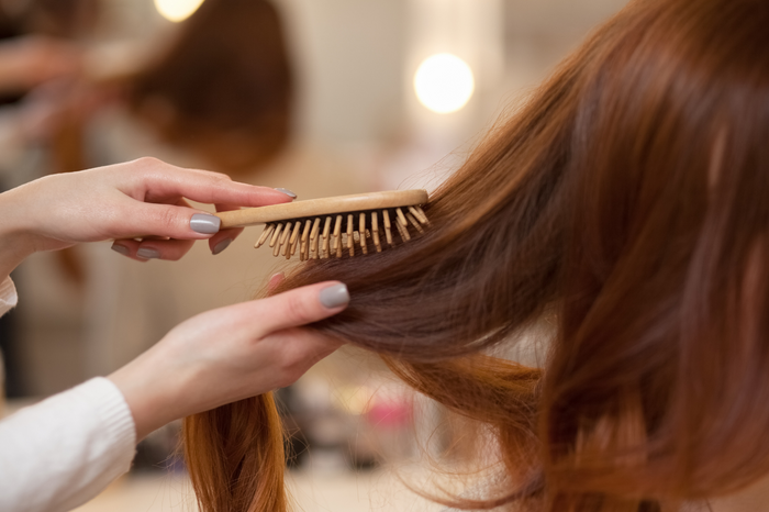 Hände bürsten langes braunes Haar mit Holzbuerste im Salon.