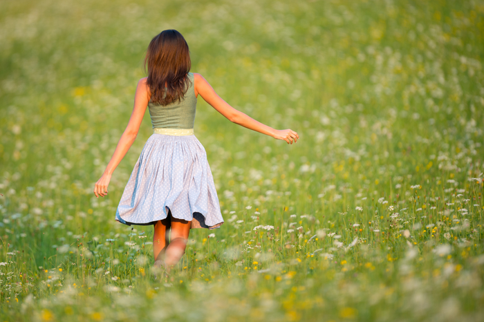 Frau in Dirndl läuft durch blühende Wiese, Rückenansicht.