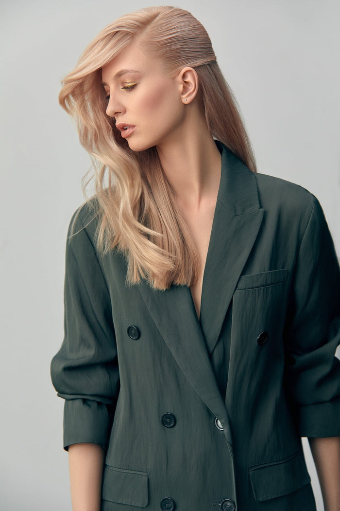 Frau mit langem, blondem Haar im asymmetrischen Styling, trägt einen dunklen Blazer.