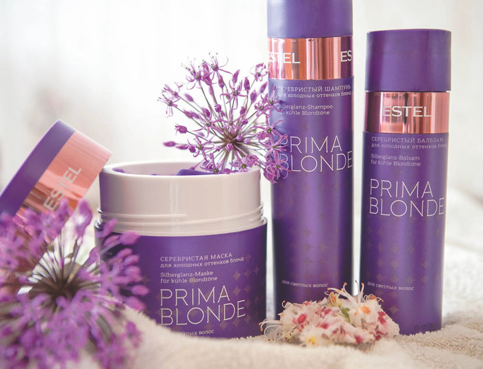 Estel Prima Blonde Serie mit Silberglanz-Shampoo, Balsam und Maske in violetten Verpackungen, dekoriert mit Blüten.