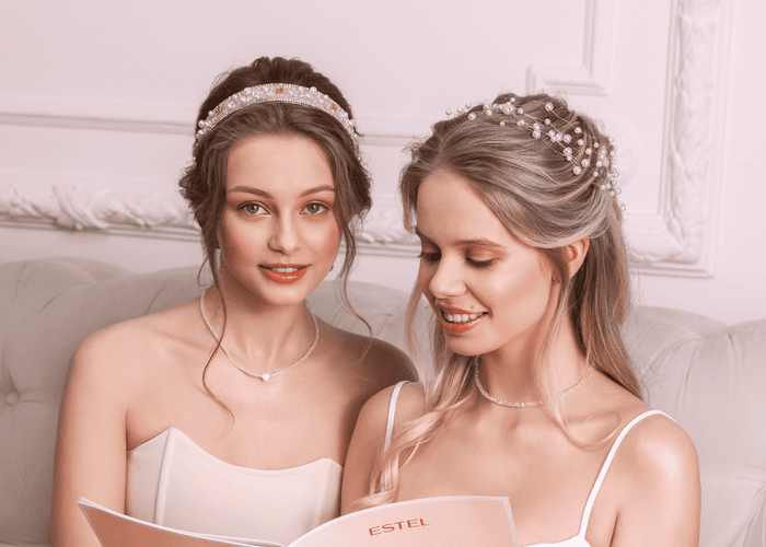 Zwei Frauen in weissen Kleidern mit Brautfrisuren und Perlenhaarschmuck.