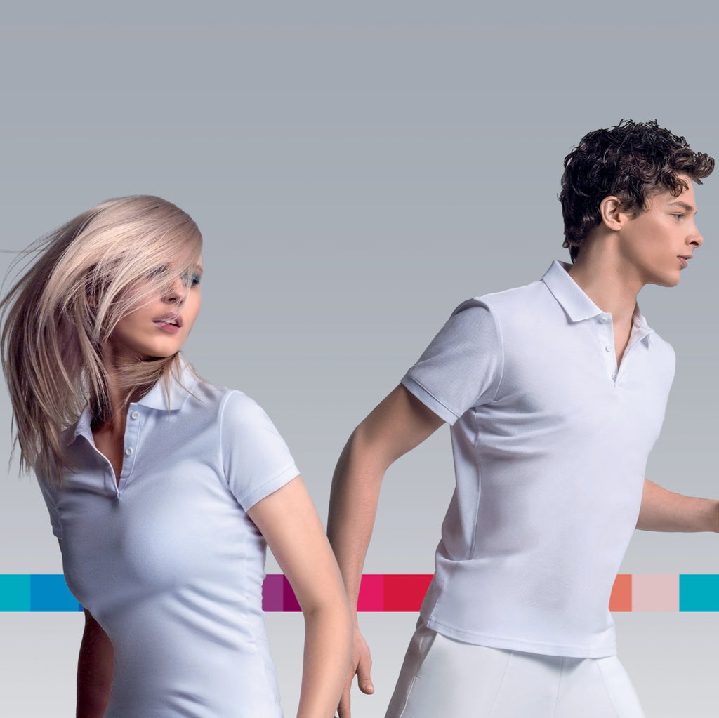 Frau mit hellblondem Haar und Mann mit dunklem Haar in weißen Shirts, dynamische Pose vor grauem Hintergrund mit bunter Farbskala – Symbol für Haarfarbenvielfalt.
