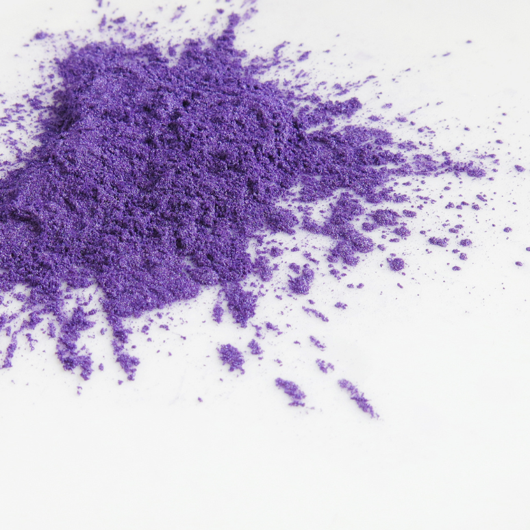Nahaufnahme von losem, violettem Farbpulver auf weißem Hintergrund, verstreut und unregelmäßig verteilt.