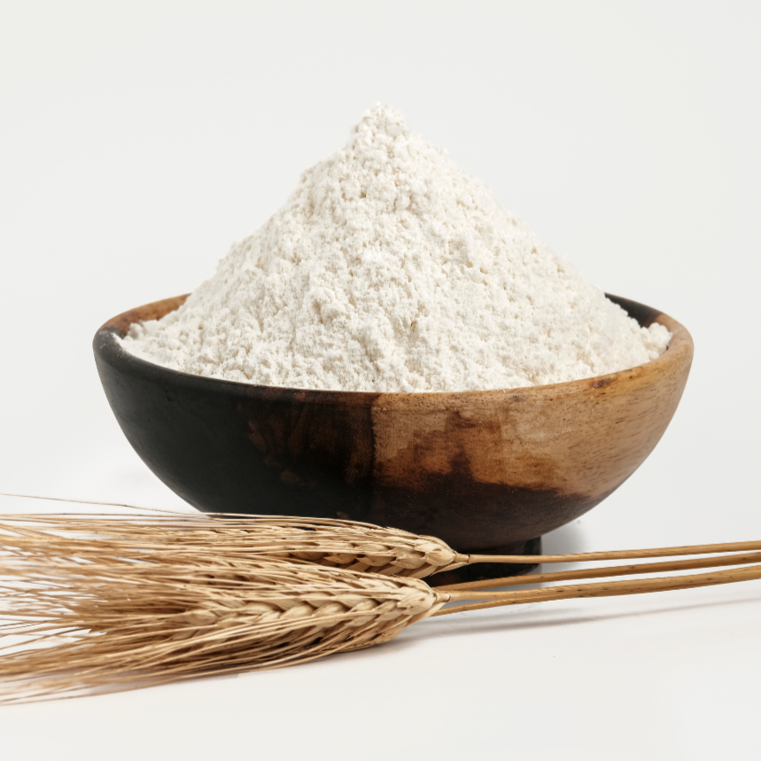 Holzschale mit weißem Pulver, davor liegende Weizenähren, auf hellem Hintergrund fotografiert.