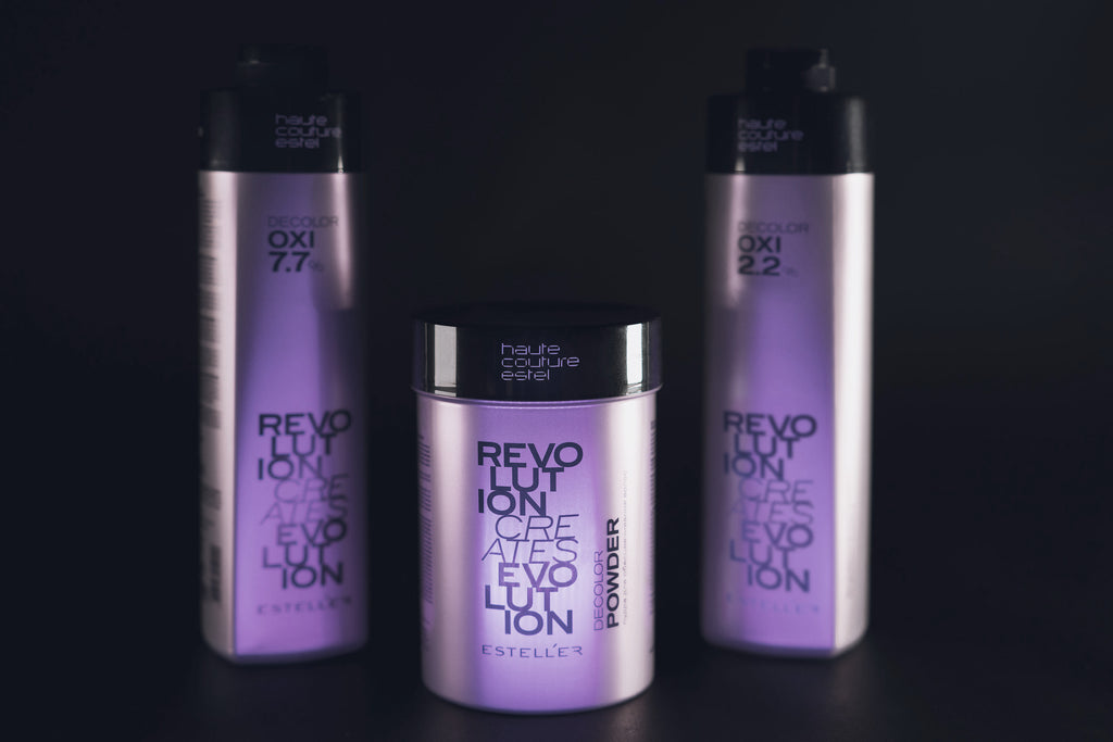 ESTEL Haute Couture Revolution Decolor Set: Zwei lilafarbene Flaschen Oxidationsmittel 7,7 % und 2,2 % sowie eine Dose Decolor Powder, vor schwarzem Hintergrund.
