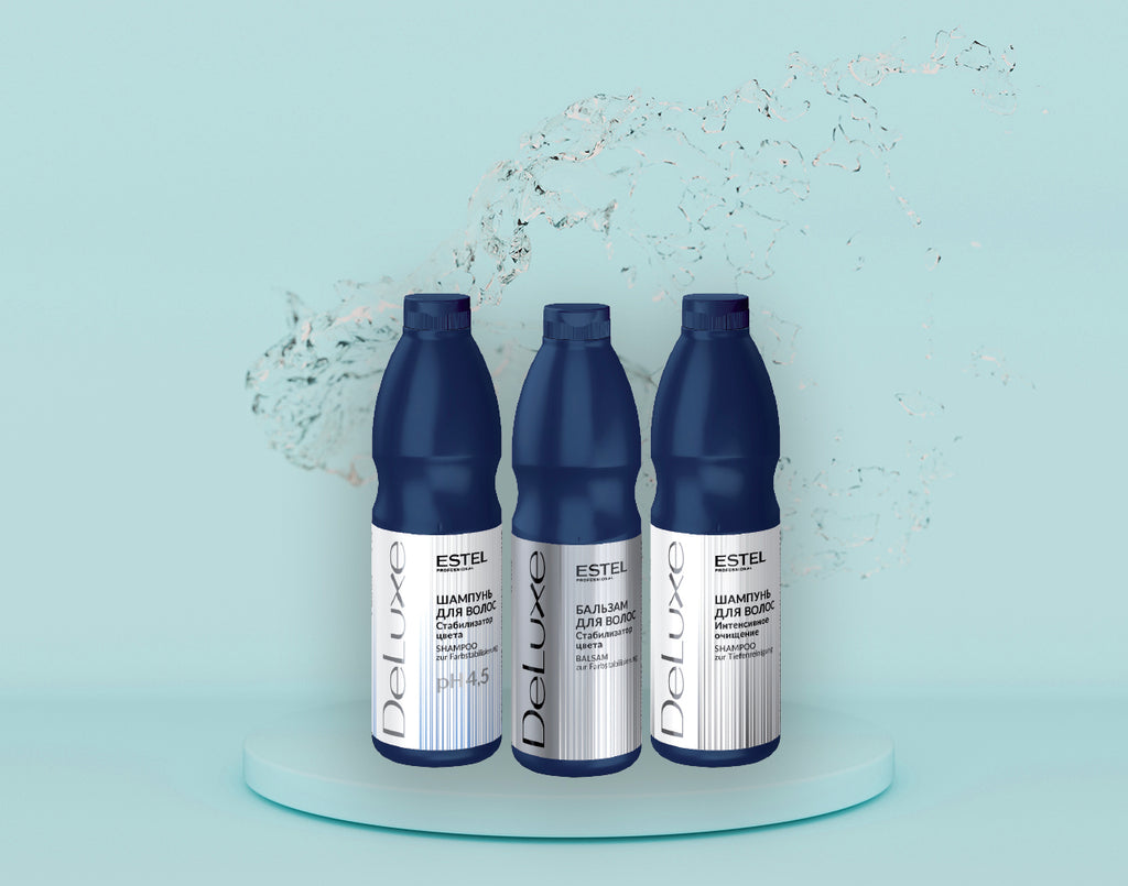 ESTEL DeLuxe Pflegeset: Drei dunkelblaue Flaschen mit Shampoo und Balsam für coloriertes Haar, auf rundem Podest vor hellblauem Hintergrund mit Wasserspritzern.