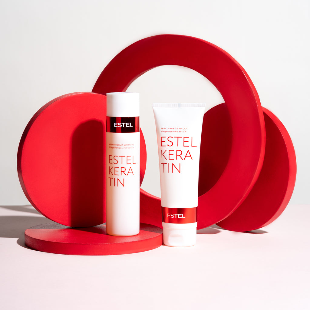Zwei ESTEL KERATIN Produkte: Shampoo und Maske in weißen Tuben mit roter Schrift, dekorativ vor roten geometrischen Kreiselementen platziert.