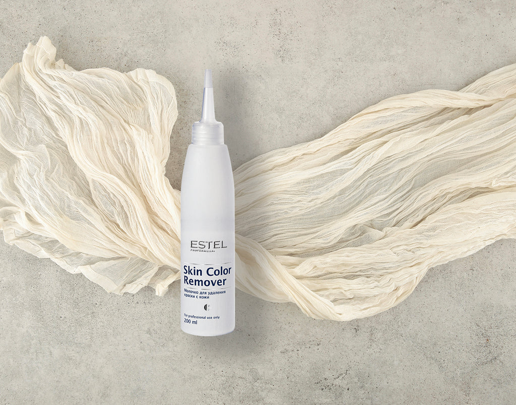 Weiße Flasche ESTEL Skin Color Remover 200 ml mit feiner Dosierspitze, auf hellem Tuch vor grauem Hintergrund arrangiert.