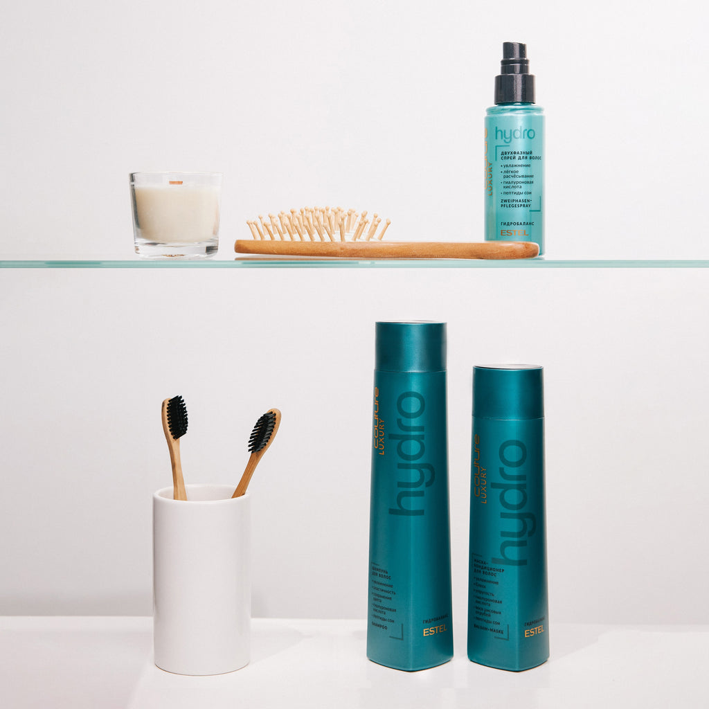 Türkisblaue Flaschen ESTEL HC LUXURY HydroBalance Shampoo, Balsam-Maske und Spray auf Glasregal, dekoriert mit Bürste, Zahnbürsten und Kerze