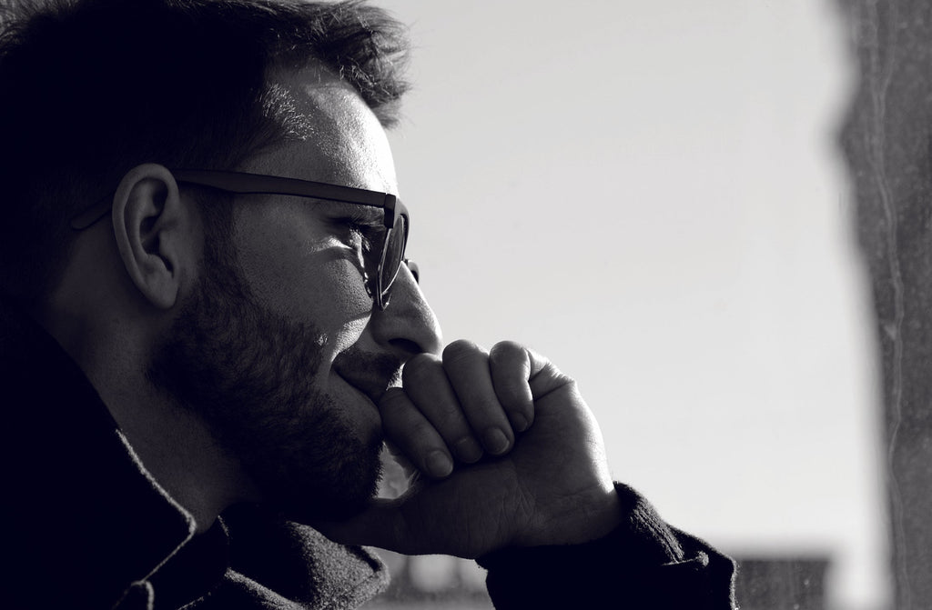 Schwarzweiß-Fotografie eines Mannes mit Bart und Sonnenbrille im Profil, nachdenklich mit Hand am Kinn