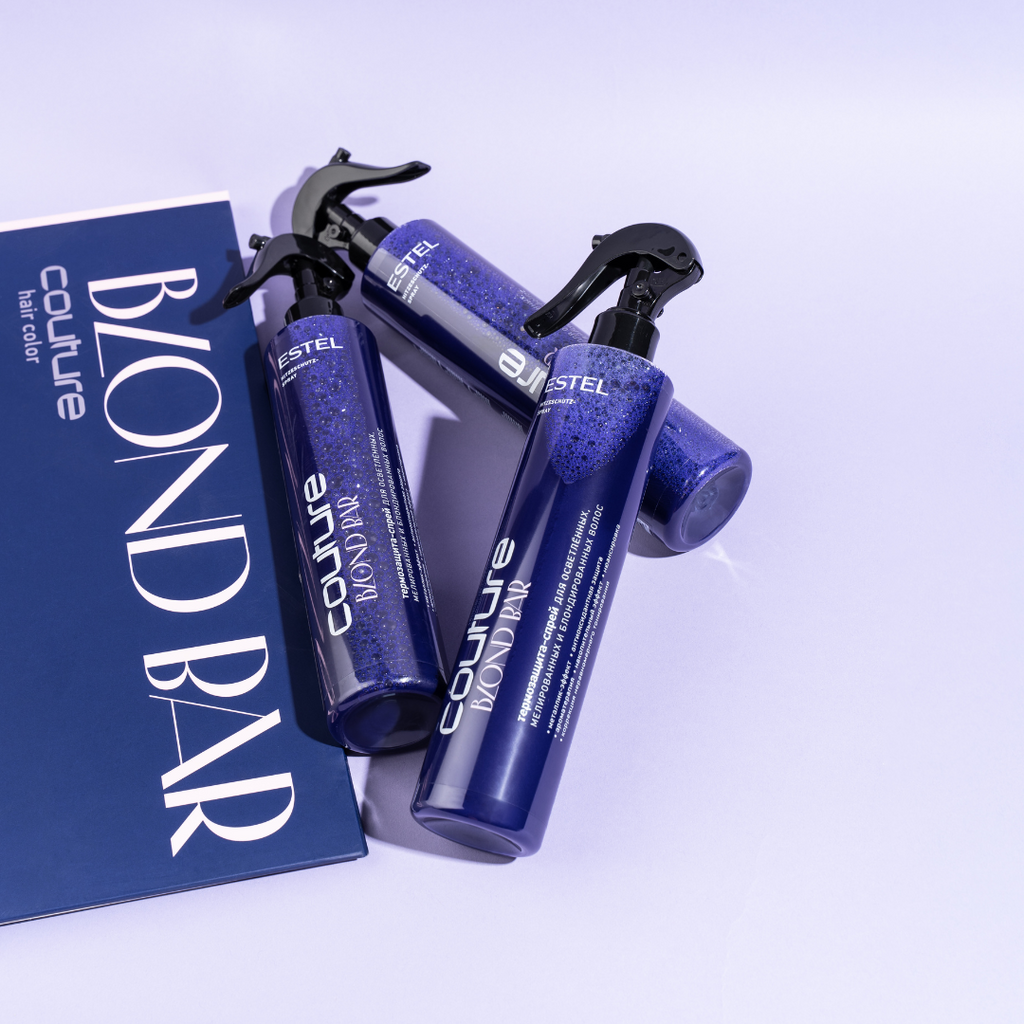 Drei dunkelblaue Sprayflaschen HC BBC Hitzeschutz-Spray liegen auf lilafarbenem Untergrund neben einer blauen Broschüre mit der Aufschrift ‚Blond Bar‘