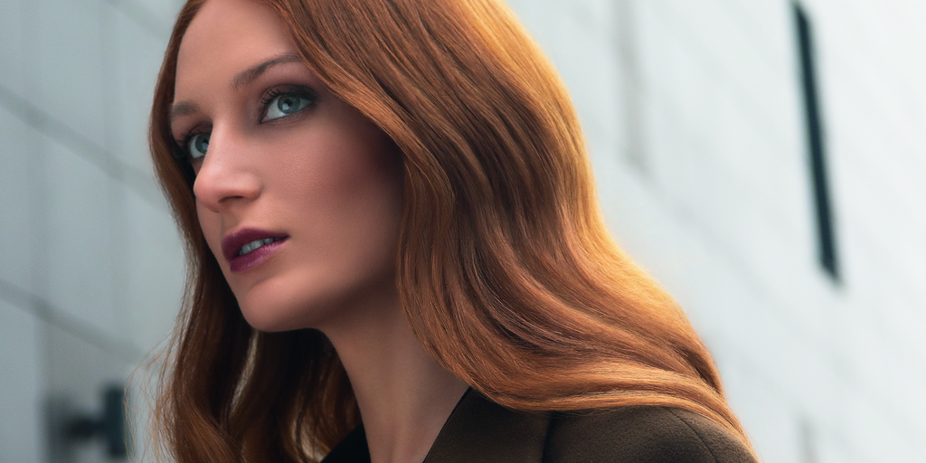 Porträt einer Frau mit langen, glatten rotbraunen Haaren und violettem Lippenstift vor hellem urbanem Hintergrund